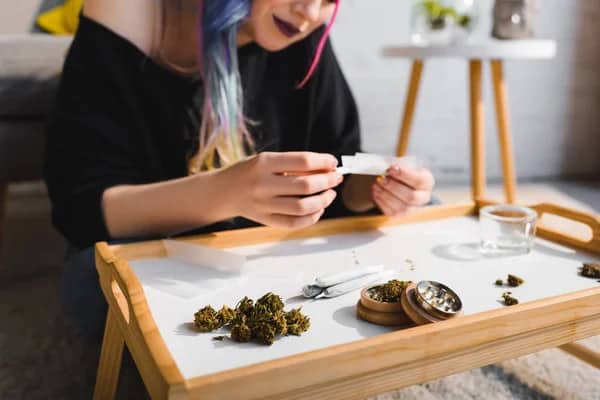 woman with colorful hair rolling joints on a small coffee table